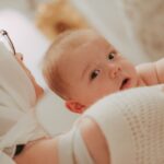 portrait of a six-month-old baby in the arms of his mother during christening looks at the camera